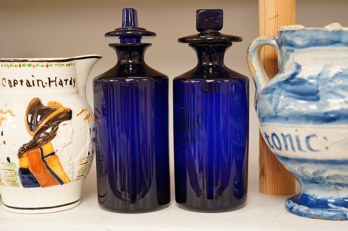 An 18th century pearlware mug, an 18th century Italian maiolica wet drug jar, a faceted wine glass, a commemorative jug and a pair of Bristol blue glass decanters and stoppers, tallest 19cm. Condition - varies